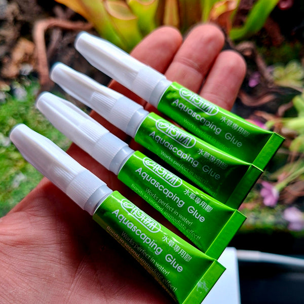 Hand holding multiple tubes of Aquascape Aquascaping gel glue tubes with a blurred natural plant background